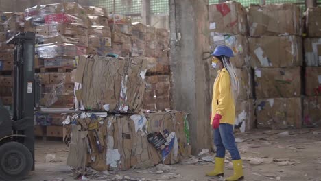descarga de papel residual en un almacén controlado por un automóvil eléctrico por una trabajadora con sombrero y chaqueta amarilla. enormes existencias de cartón prensado. cámara lenta