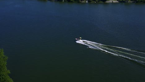 Un-Dron-Sigue-Una-Lancha-Rápida-Familiar-Que-Tira-De-Dos-Personas-Que-Practican-Wakeboard-En-El-Agua-Del-Lago-Killarney-En-Turtle-Mountain,-Al-Suroeste-De-Manitoba,-Canadá.