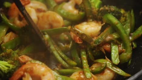 unrecognizable person stirring with tweezers the pan with shrimps