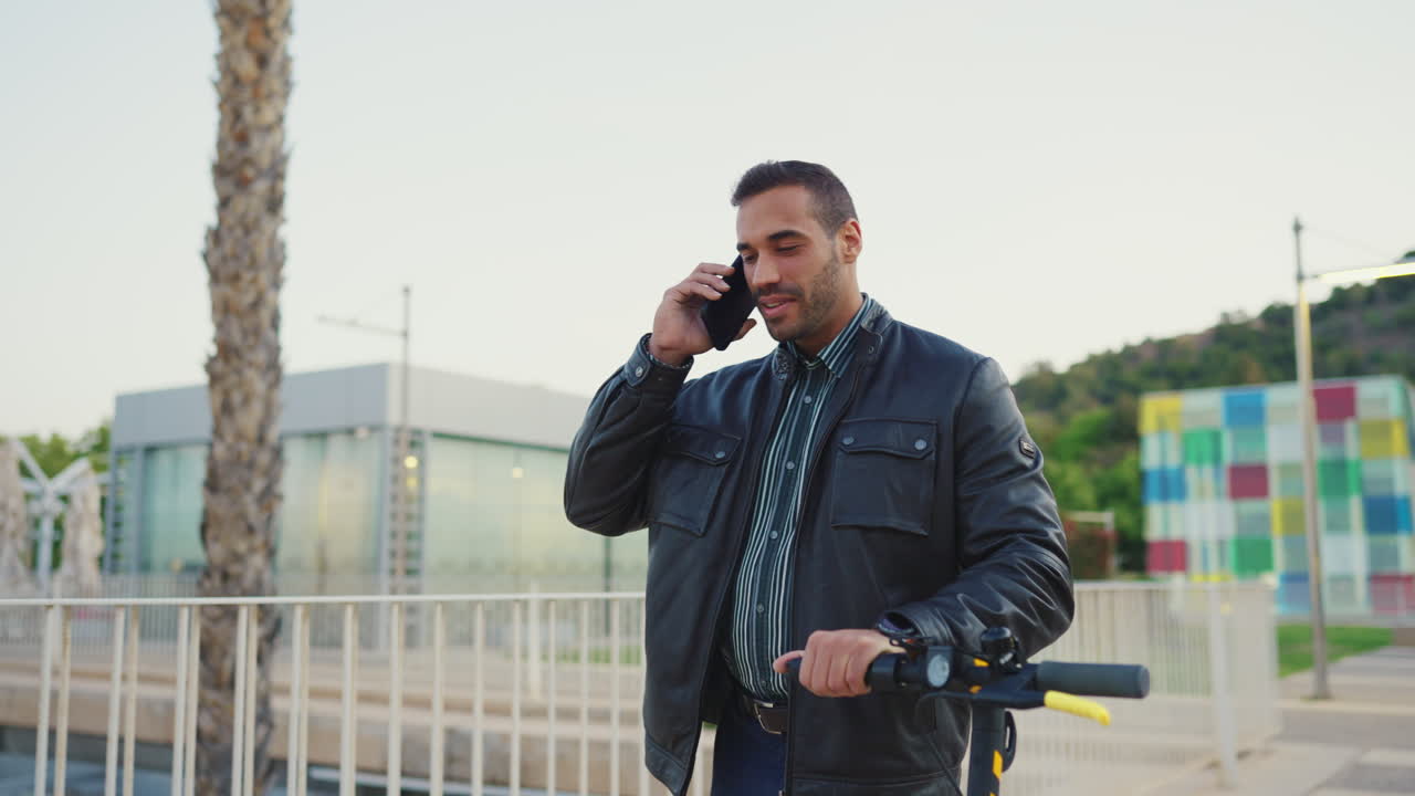 Dışarıda scooter'ıyla akıllı telefondan konuşan genç adam.