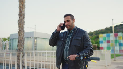 young man with scooter calling on smartphone outdoors.