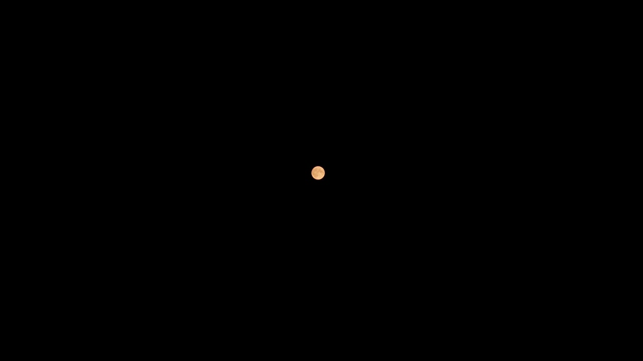 Orange full moon illuminating the dark night sky above the city of Kaunas, Lithuania, creating a mystical and serene atmosphere filled with wonder and beauty