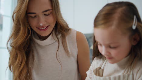 Playful-child-touching-mother-nose-kitchen-close-up.-Woman-and-girl-having-fun