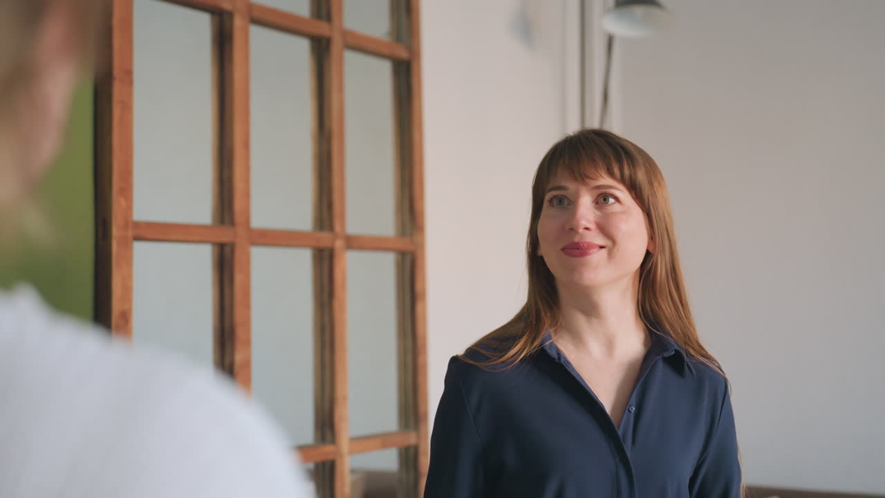 Over shoulder view of patient facing smiling specialist who warmly gestures toward sofa during session, soft light enhances warm welcoming atmosphere in comfortable professional environment