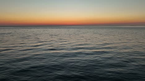 aerial shot pulling up and away from the sun setting with a warm glow over the ocean