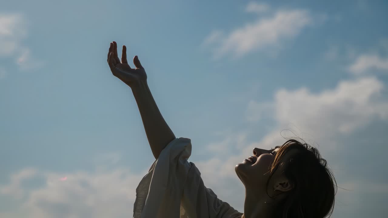 Raising right arm, woman turning, smiling to sky over field, wearing light blouse, sun warming face