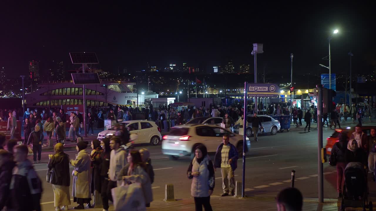 escena nocturna en estambul con multitudes de personas, coches y un autobús en la calle.