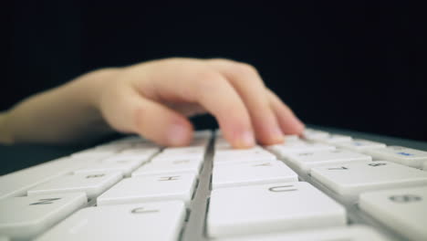 child presses keys on modern computer keyboard in dark space