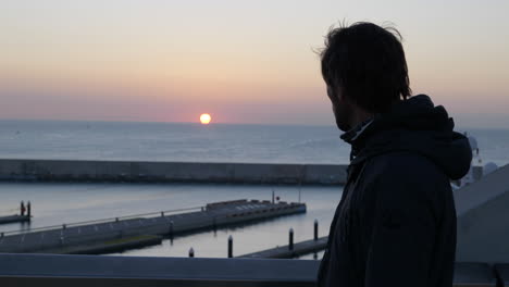 Casual-man-walking-Barcelona-marina-bridge-alone-watching-the-sunset-over-the-ocean