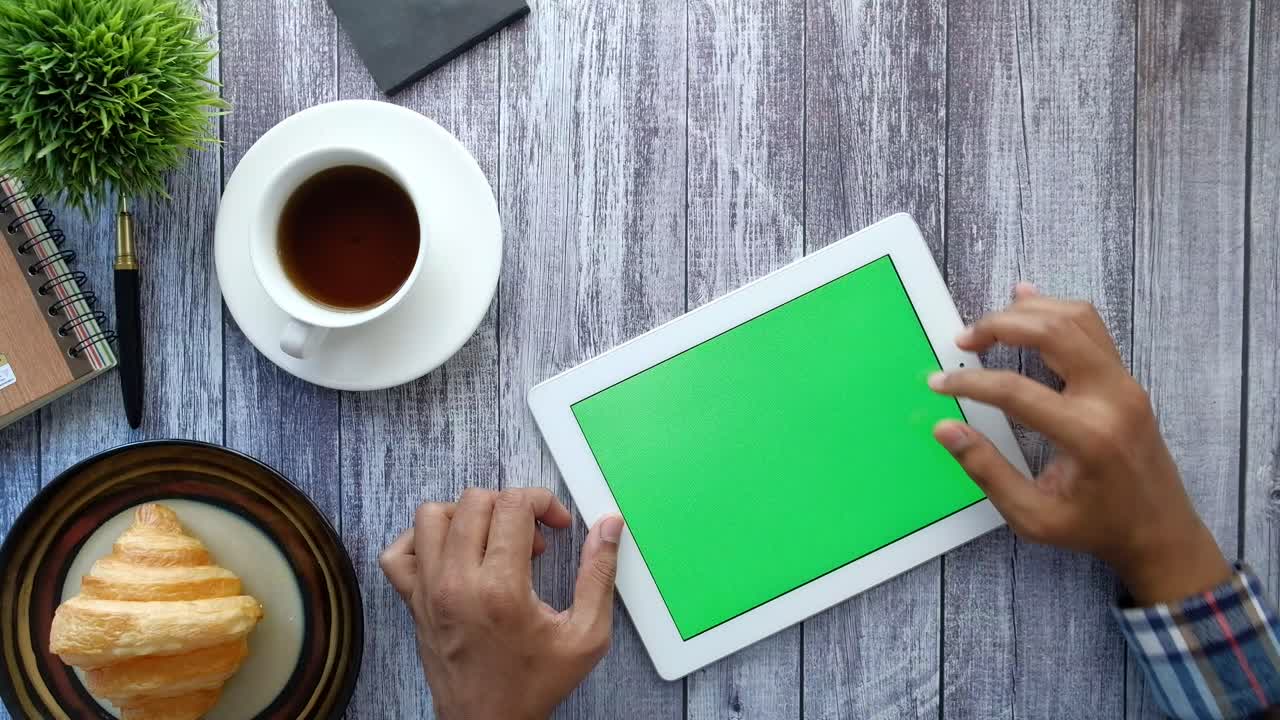 persona que usa una tableta con pantalla verde, desayuno y café en la mesa