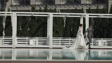 newlyweds caucasian bride groom walking near swimming pool, holding hands, wedding couple family