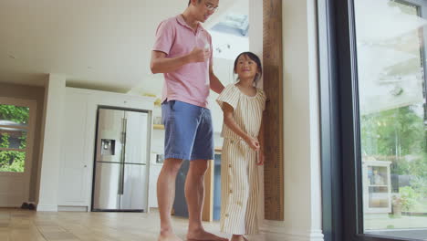 Padre-Asiático-Midiendo-A-Su-Hija-A-Escala-De-Pared-En-Casa-Mientras-Ella-Se-Pone-De-Puntillas