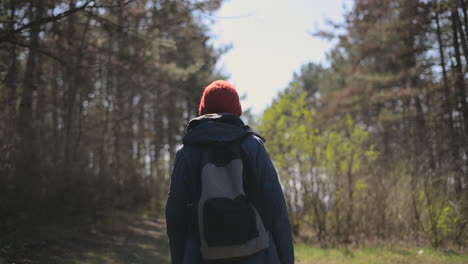 an unrecognizable young woman in a red woolen hat walks through the forest looking from side to side 1