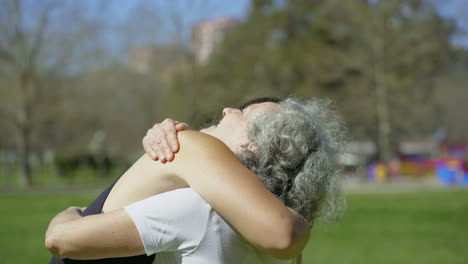 una mujer mayor sonriente abrazándose con una joven deportiva en el parque.