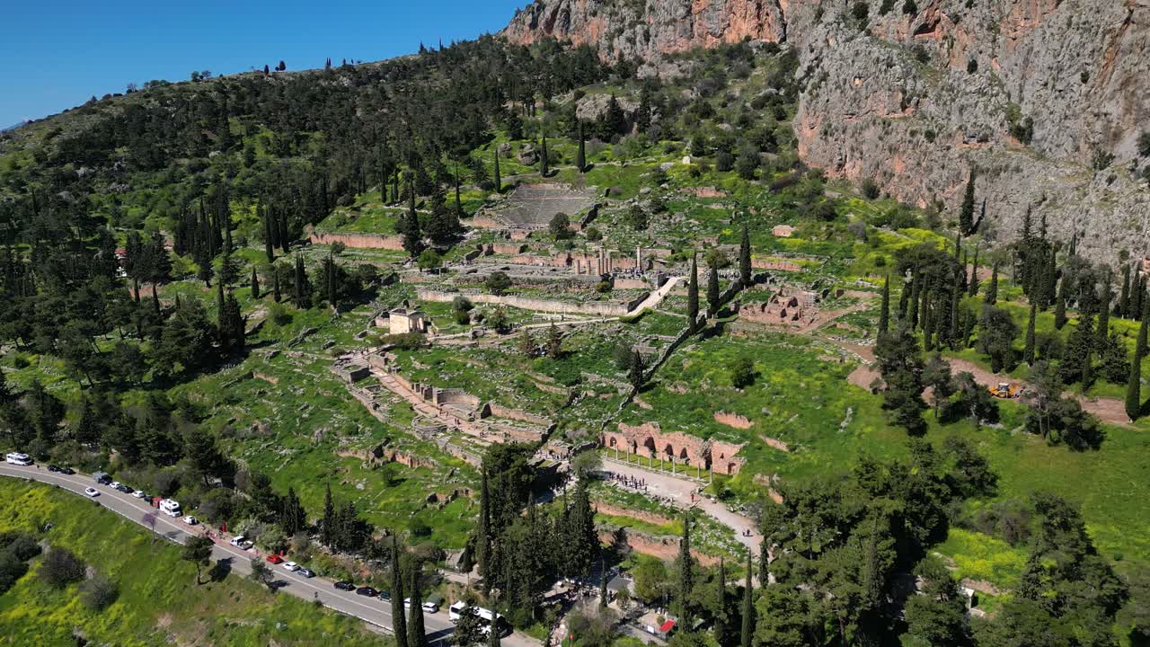 Aerial orbit of Delphi archaeological site with ruins, trees, and sloped mountain terrain