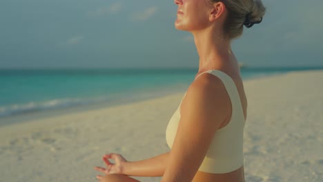 attractive woman in sports wear meditating on beach in easy pose at sunrise