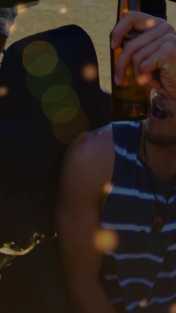 Video verticale: Uomo in canottiera che solleva una birra dopo aver passato la bottiglia, bokeh di viaggio rilassante che mostra uno spruzzo.