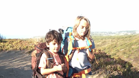 active kids walking on mountain path, carrying heavy backpacks