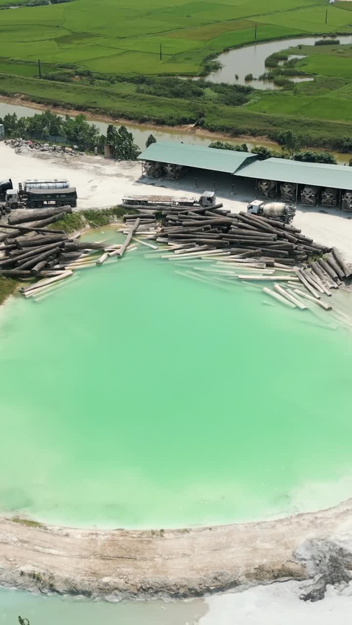 Logs in water with trucks and building in background