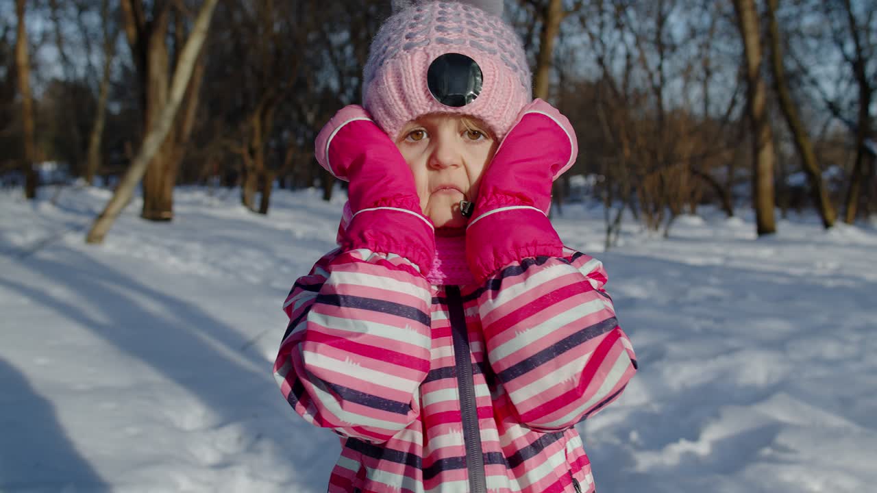 A young girl smiles while wearing pink winter clothes in a snowy forest