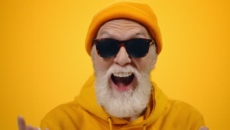 old man having fun indoor. joyful guy gesticulating on yellow studio background.