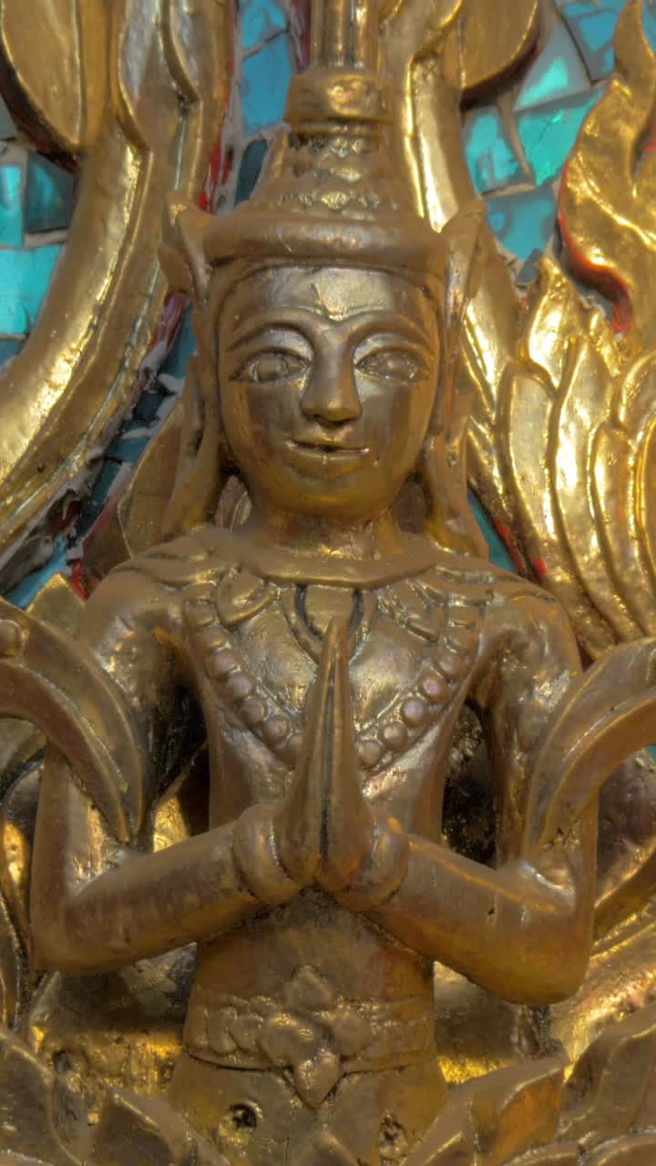 Primo piano di una statua religiosa dorata e ornata in posa di preghiera.