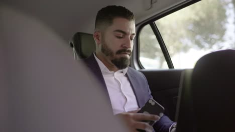 focused businessman using smartphone and laptop in car