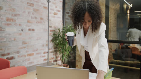 biracial businesswoman with takeaway coffee standing at desk looking at document, in slow motion