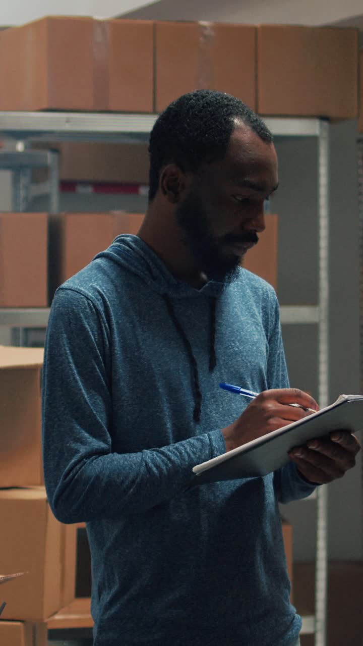 Vertical video: Male entrepreneur taking inventory notes on clipboard files