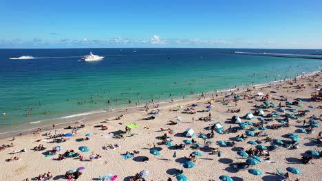 drone clip over busy golden beach with people sunbathing and colourful umbrellas, with blue green open sea and cruise ship in the background