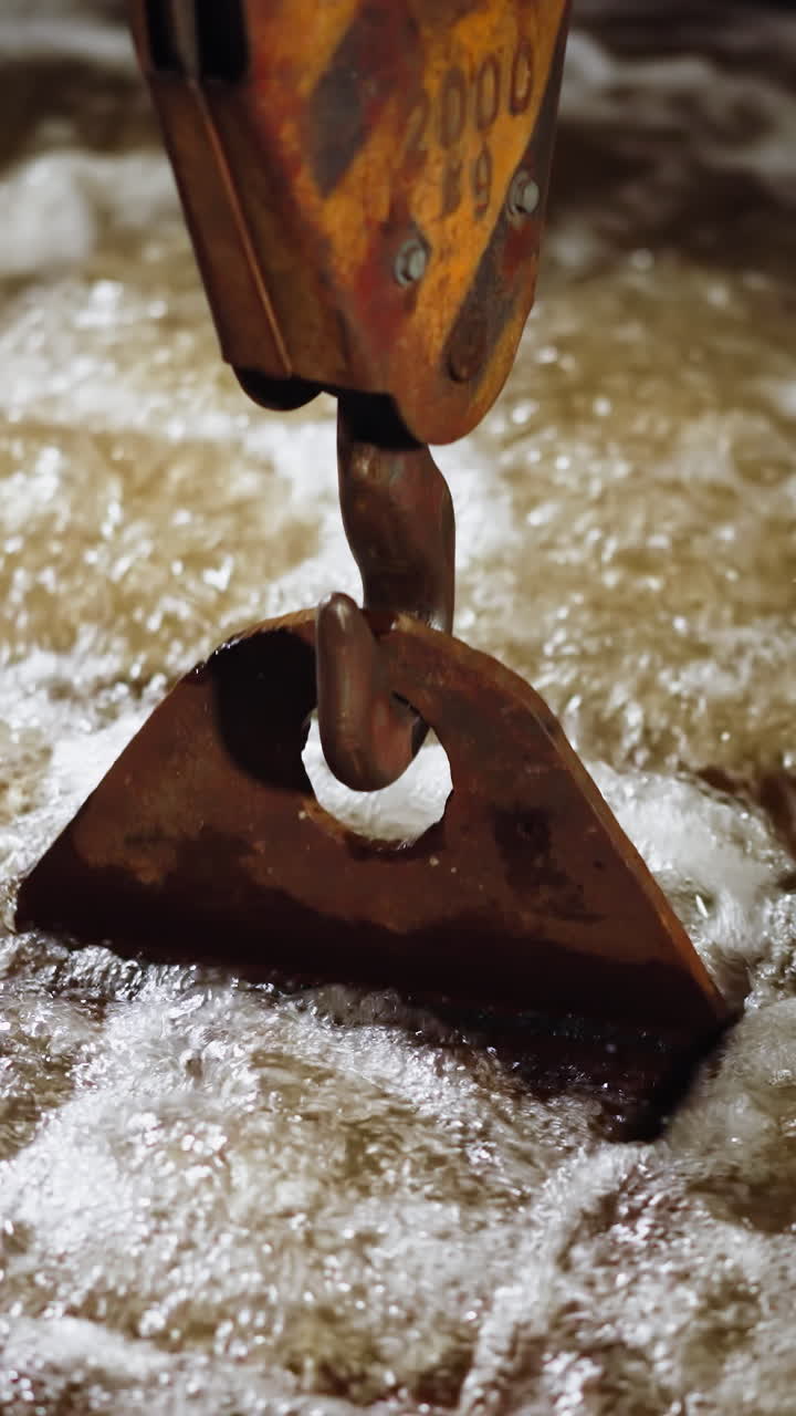 el gancho de la grúa sumergido en agua espumosa en un proceso dinámico de sofocamiento industrial de metales