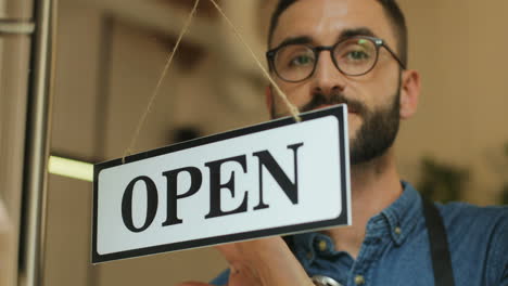 Close-up view of young man turning over a open" signboard in coffee shop door"