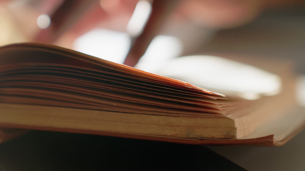 Primo piano sfocato di una persona che tiene in mano un libro con pagine leggermente usurate e illuminazione calda, che cattura la delicata curva dei bordi della carta e la sottile texture