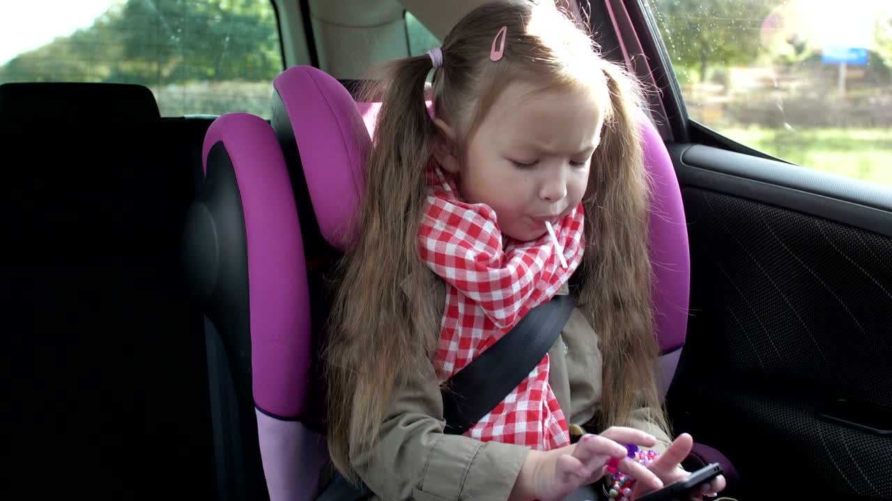 una niña linda ocupada con su teléfono inteligente mientras está sentada en el asiento trasero del coche. un niño de edad primaria encantador jugando en el teléfono celular durante un viaje por carretera