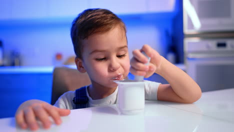 adorable caucasian toddler sitting at the table eating yogurt. lovely baby boy enjoying dairy. close up.