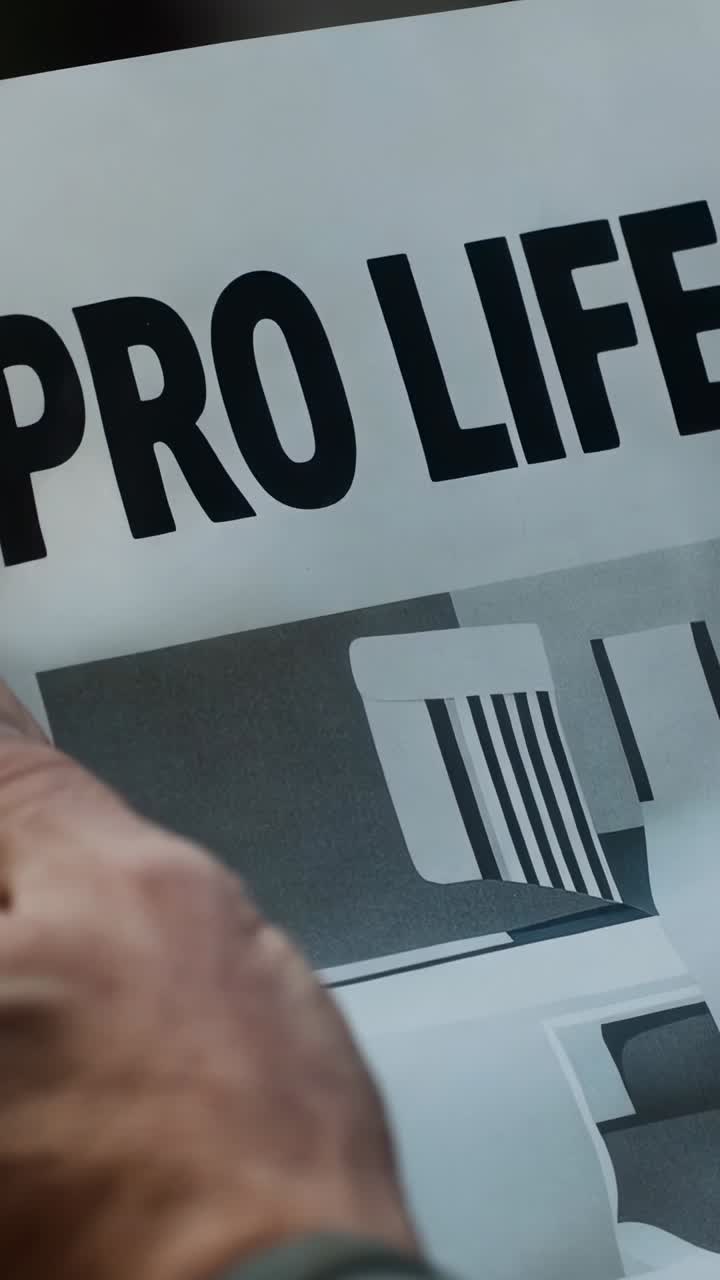 Vertical video: Entering from left, bare forearm gripping placard in close-up, displaying PRO LIFE