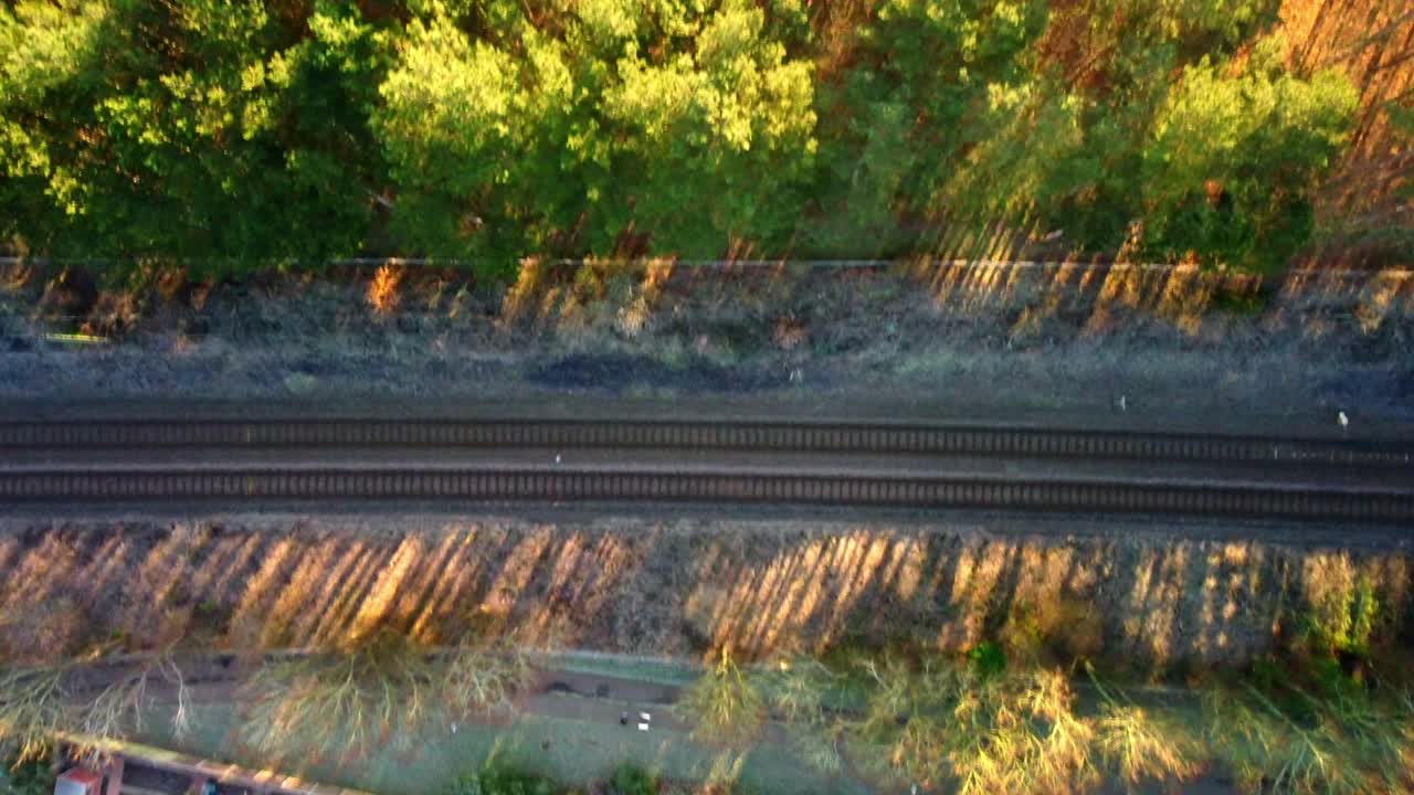 Bird eye footage off a train line with trees surrounding and the sun shining through the trees creating interesting stretched out shadows.