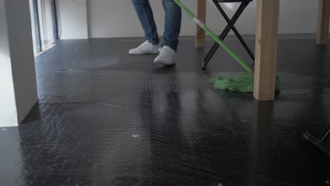hombre trapeando el piso debajo de la mesa en el lugar de trabajo