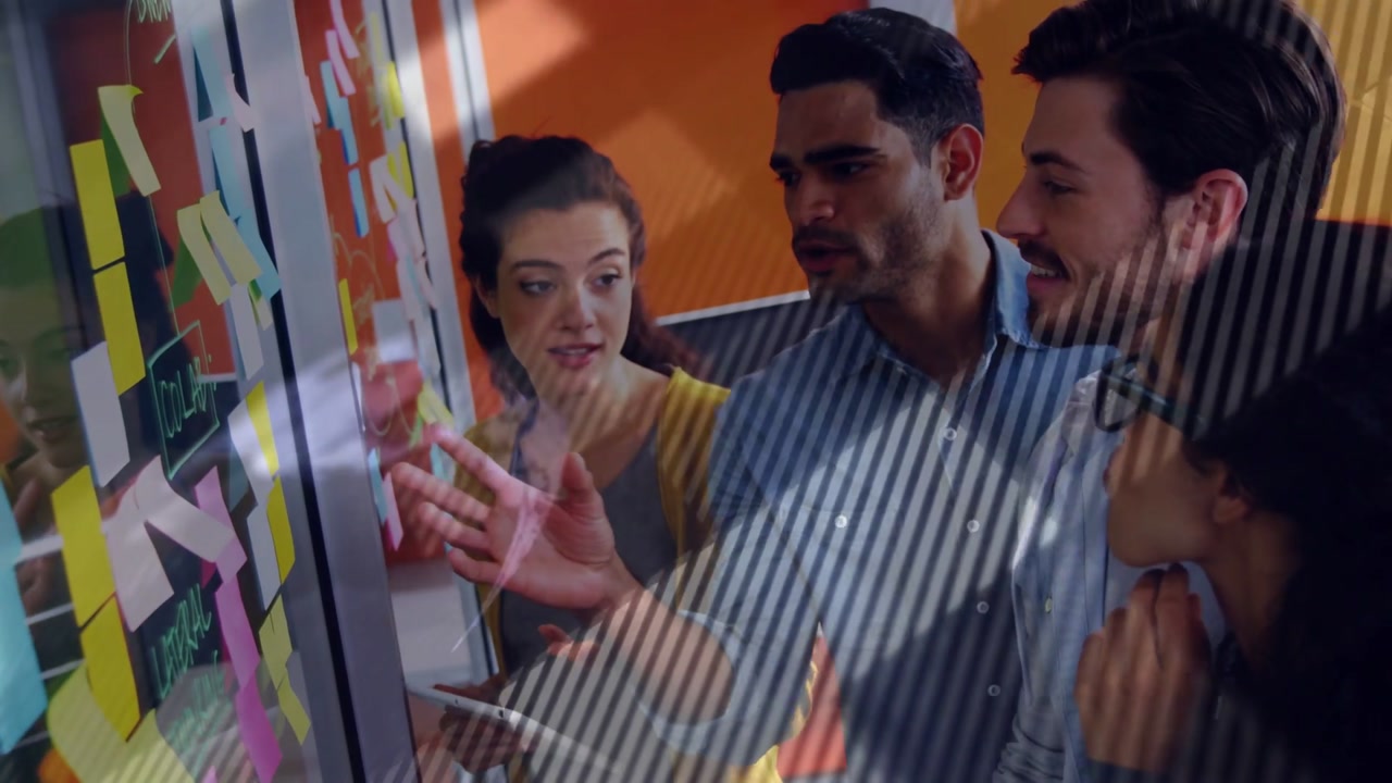 Woman holding tablet scanning sticky notes, man pointing while team planning business on glass
