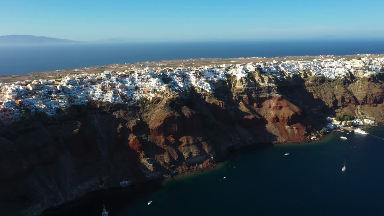 Aerial wide view of famous greek village Oia with white cave houses, villas and cliffs above Mediterranean Sea in Santorini, Greece.