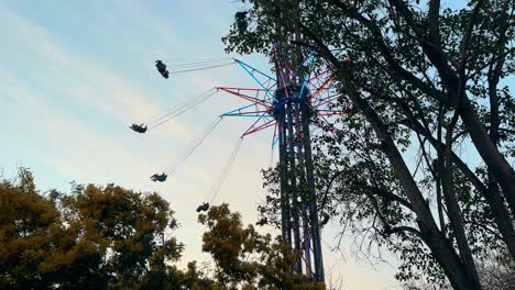 amusement park game, colorful spinning high chairs in the middle of trees, sunset in the background. santiago, chile