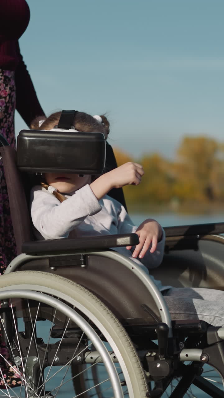 niño se sienta en silla de ruedas al lado de la madre jugando a un juego digital con gafas de realidad virtual. niña en edad preescolar inspecciona la nueva ubicación del juego en un fondo borroso
