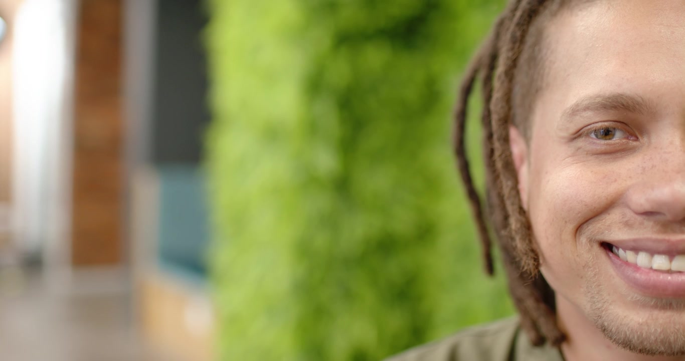 African American man in olive-top smiling at offscreen cue by plant wall in lounge, copy space