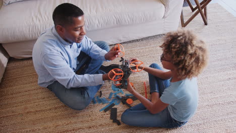 pre-teen african american girl and grandad sitting cross legged on the floor constructing a toy, elevated view