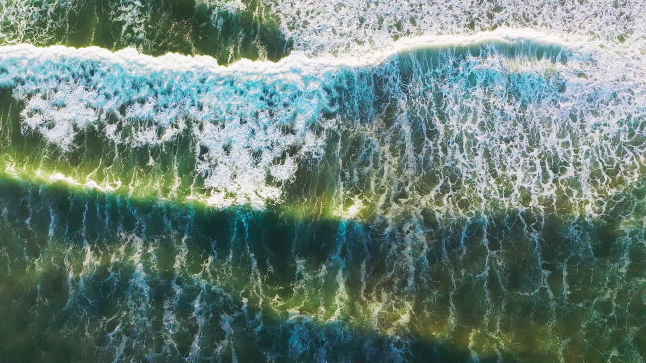 Green waters of the beautiful ocean with quickly moving waves. Following the foamy waves moving to the shore. Top view.