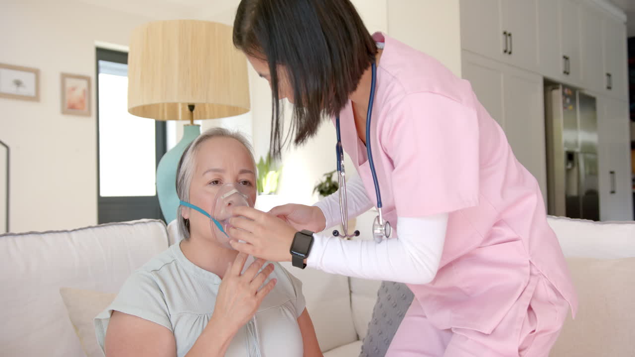 Nurse assisting senior asian woman with oxygen mask during home healthcare session
