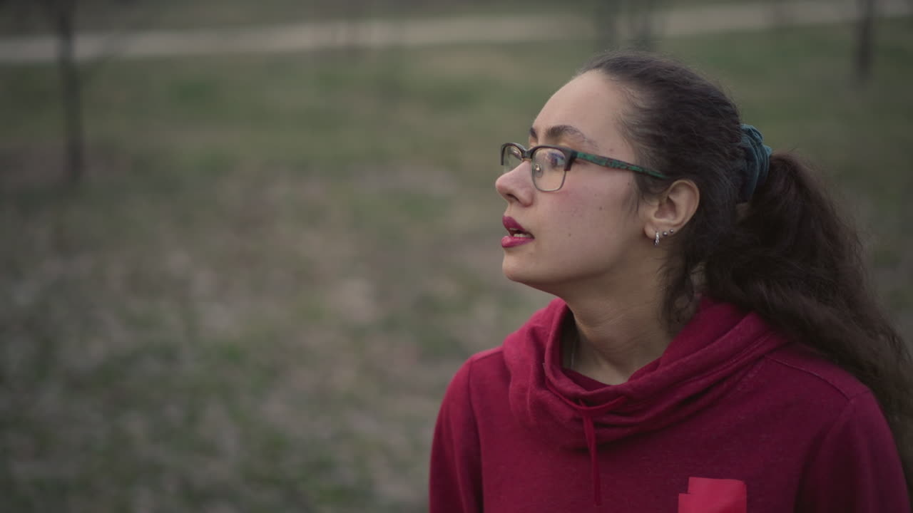 Young Woman On Country Trail, Female In Scarlet Hoodie Standing Attentively Outdoors During Overcast Evening, Young Woman Dressed In Red Hoodie Gazing Along Rural Path On Cloudy Evening Outside
