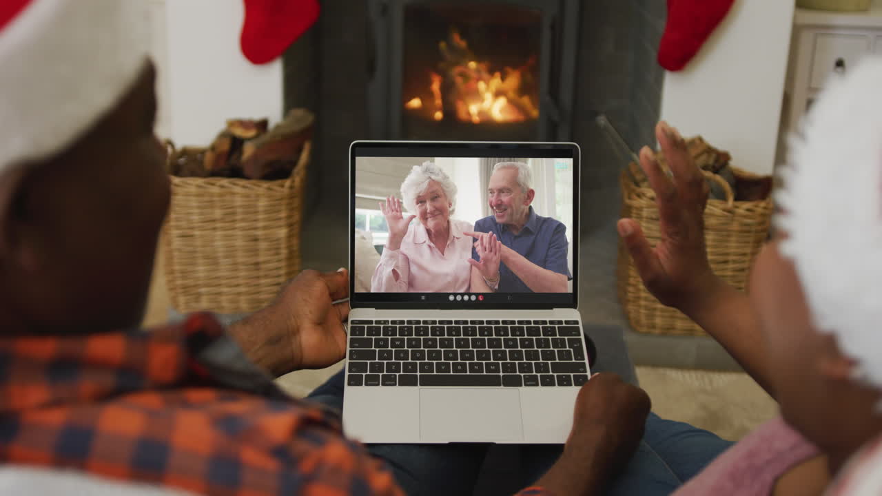 pareja afroamericana con sombreros de santa usando una computadora portátil para una videollamada de navidad con la pareja en la pantalla