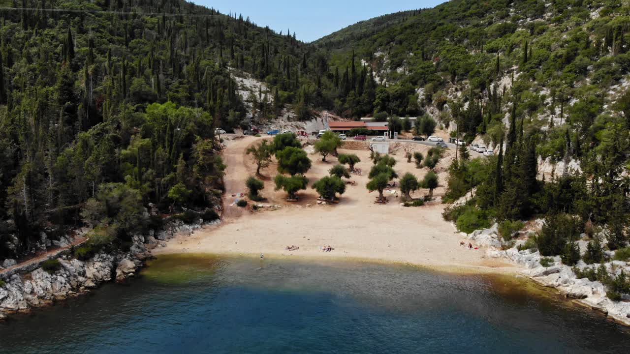 edificio de restaurante entre la montaña boscosa verde y la costa de arena en la playa de foki, grecia