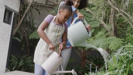 madre feliz diversa con la hija regando plantas en el jardín en cámara lenta.